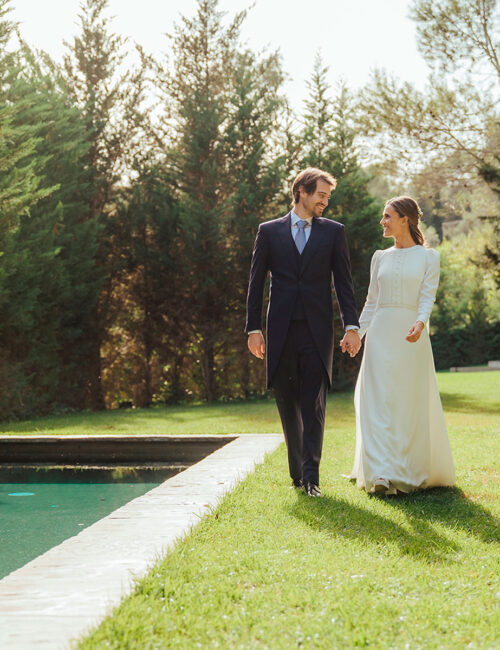 Pareja de novios paseando de la mano por el jardín al lado de la piscina